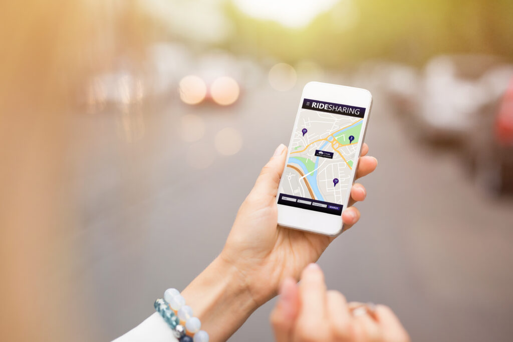 A person holds a smartphone displaying a map application, likely for ride-sharing or navigation, with a blue square and white checkmark visible in the upper right corner.